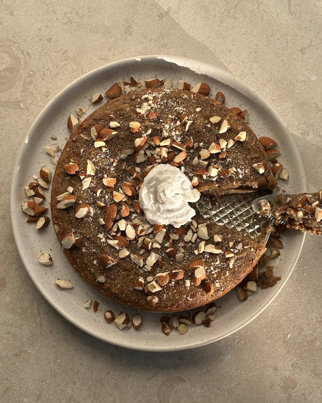 Vitt fat med en semmelkladdkaka utan vitt mjöl och socker som är toppad med hackade mandlar och en klick kokosgrädde