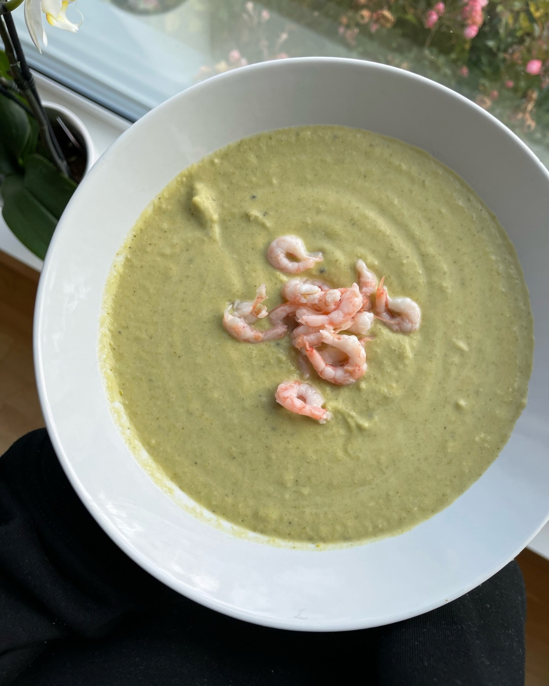 Vit skål med näringsrik krämig broccolisoppa med parmesan som är toppad med räkor