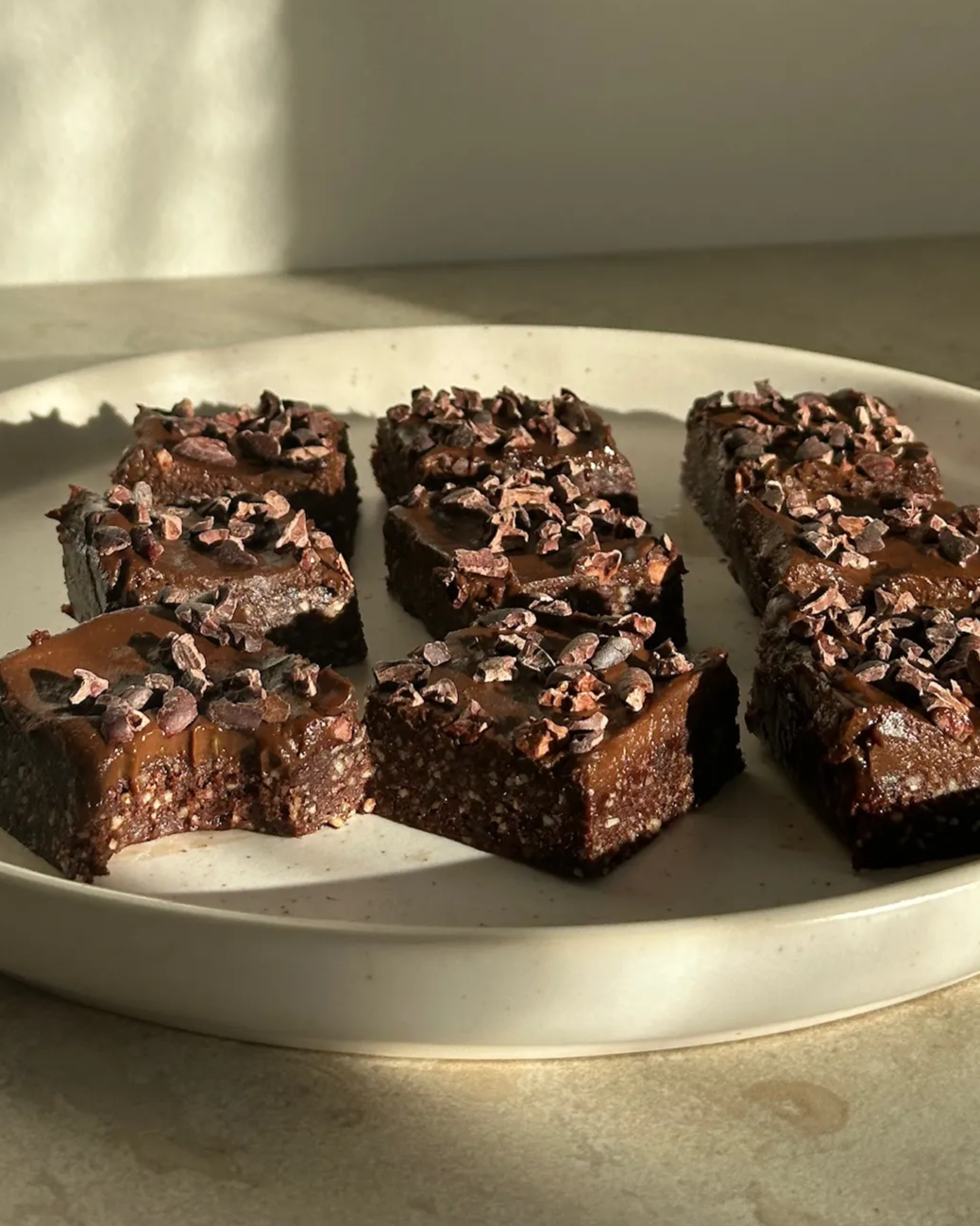 Vitt fat med mjölkfria, sockerfria och glutenfria brownies toppade med chokladfrosting och kakaonibs