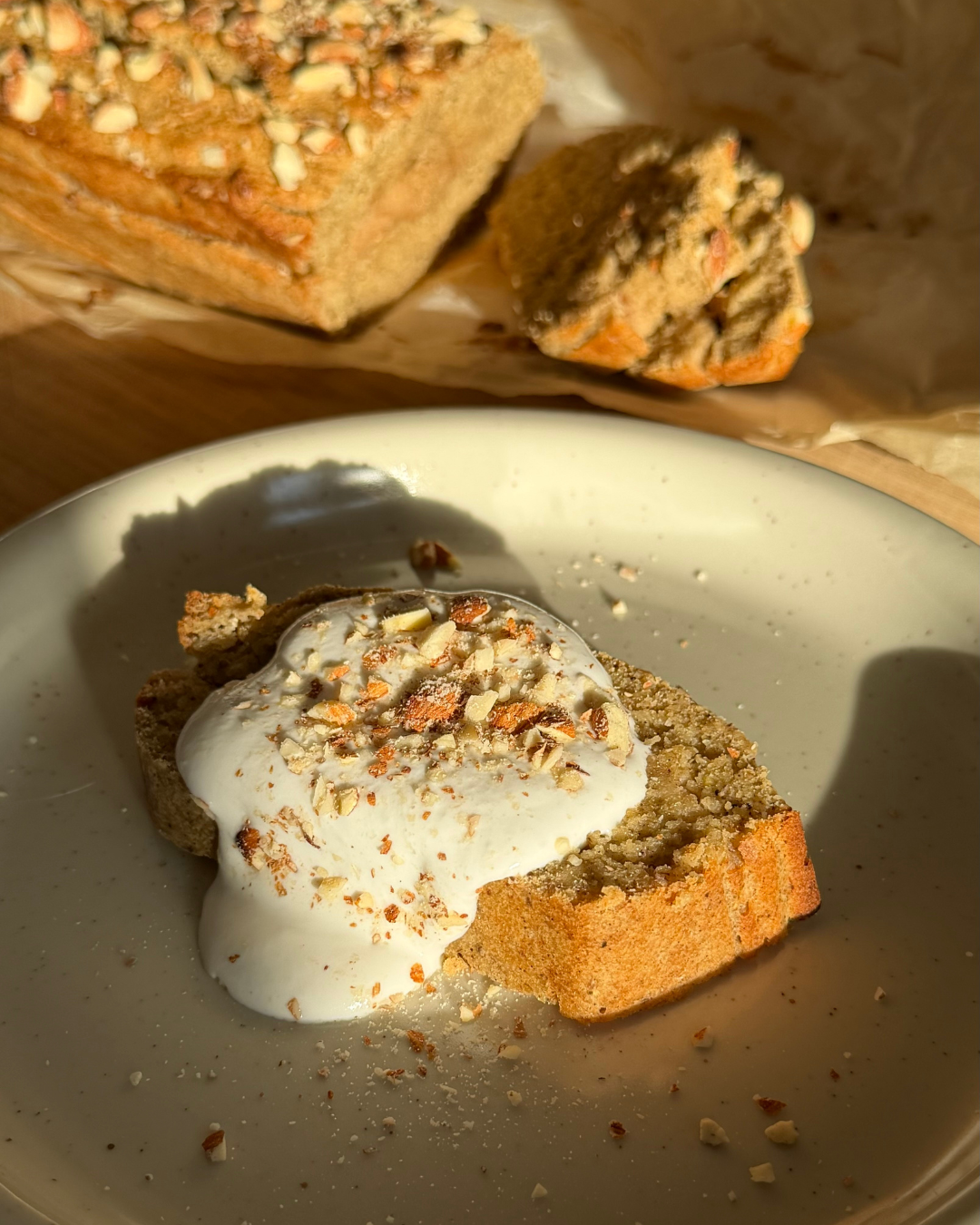 vitt fat med en skiva sockerfritt och glutenfritt semmelbananbröd med kokosgrädde och hackade mandlar på toppen